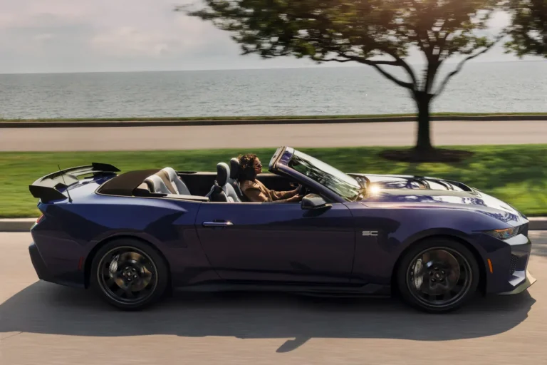 Purple Ford Mustang Dark Horse SC convertible driving beside the water with its roof lowered